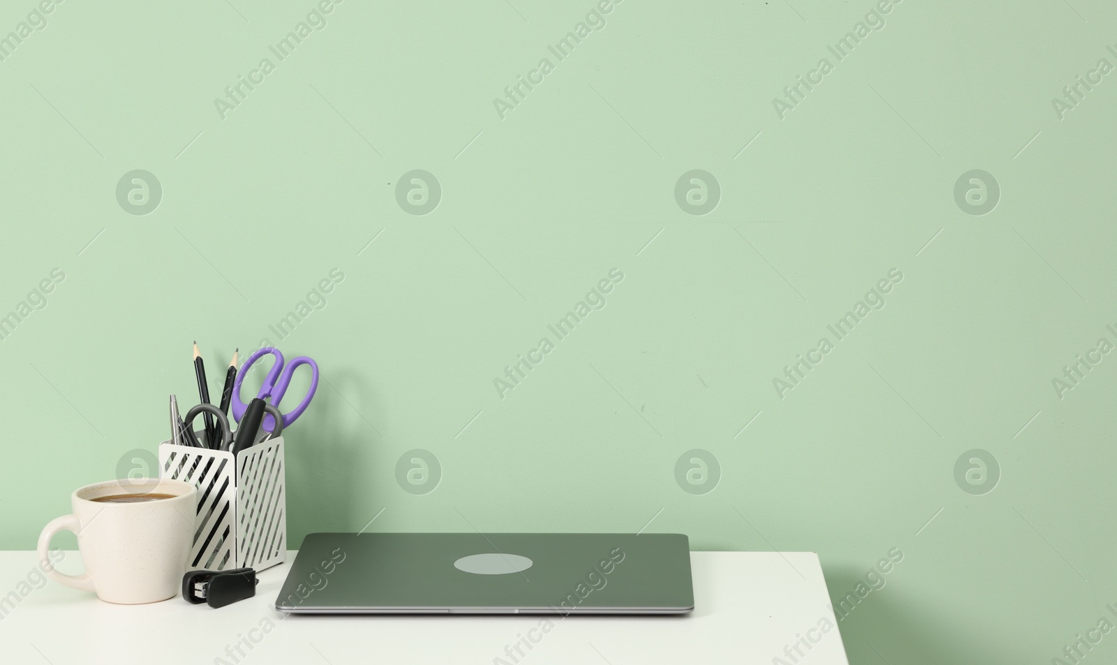 Stylish workplace with modern laptop on white desk near light green wall. Space for text Photo of Stylish workplace with modern laptop on white desk near light green wall. Space for text