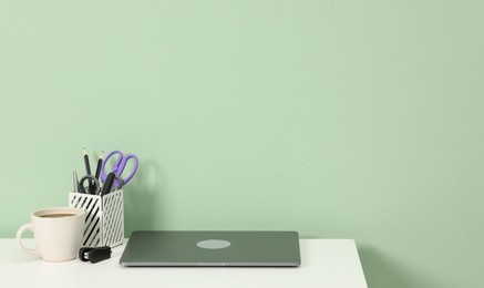 Photo of Stylish workplace with modern laptop on white desk near light green wall. Space for text