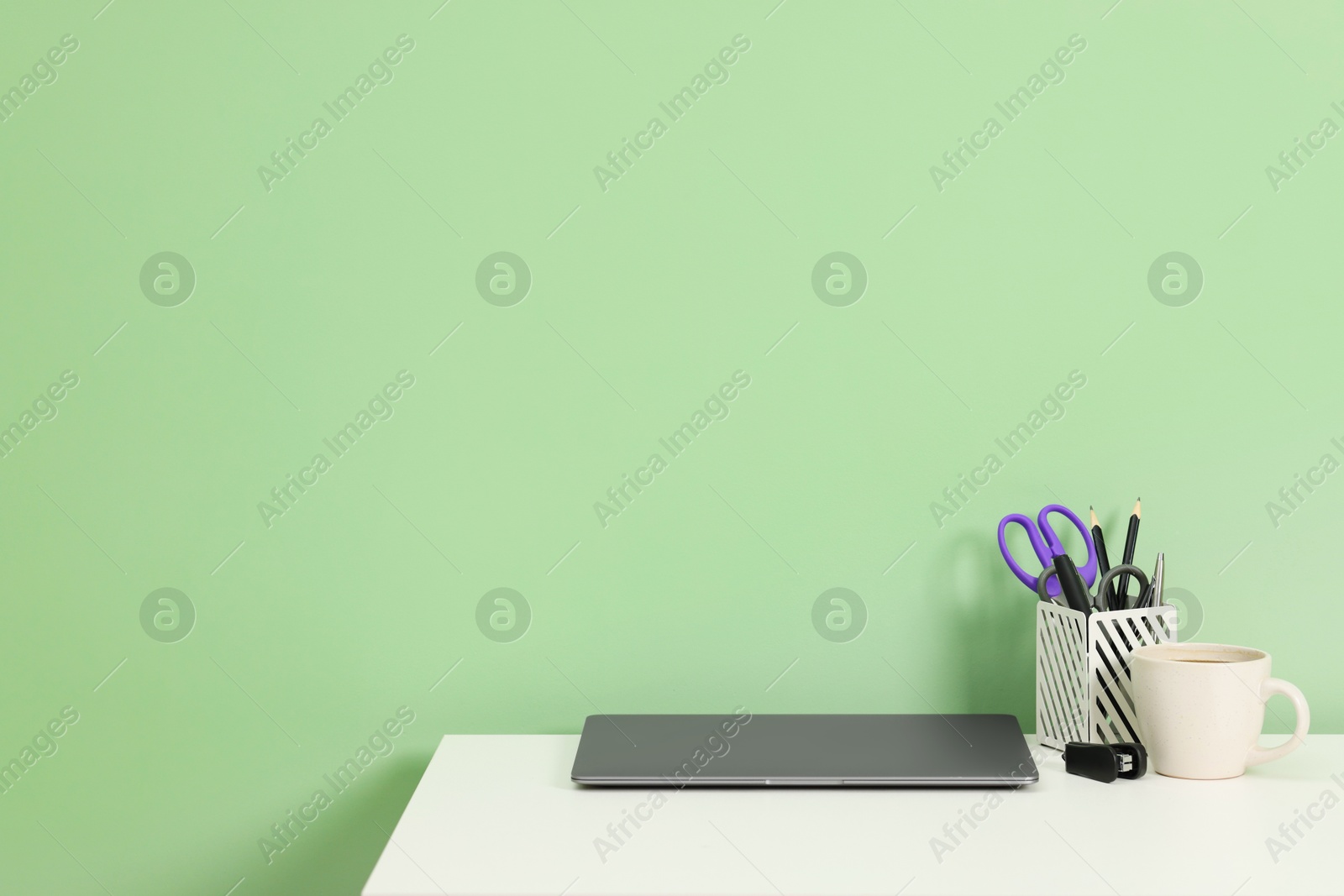 Stylish workplace with modern laptop on white desk near light green wall. Space for text Photo of Stylish workplace with modern laptop on white desk near light green wall. Space for text