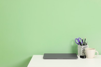 Photo of Stylish workplace with modern laptop on white desk near light green wall. Space for text