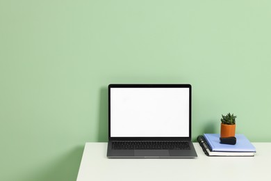 Photo of Stylish workplace with modern laptop on white desk near light green wall. Space for text