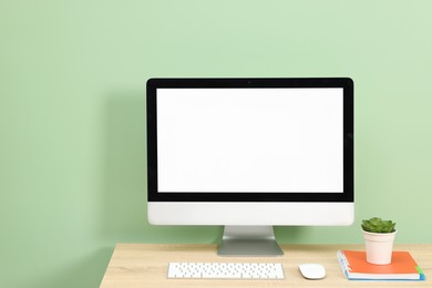 Photo of Stylish workplace with modern computer on wooden desk near light green wall