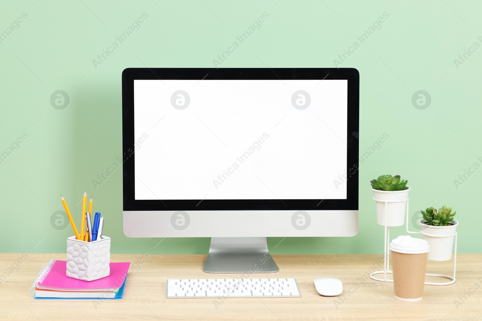 Stylish workplace with modern computer on wooden desk near light green wall Photo of Stylish workplace with modern computer on wooden desk near light green wall