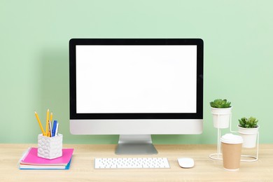 Photo of Stylish workplace with modern computer on wooden desk near light green wall
