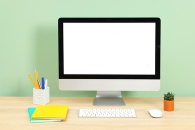Photo of Stylish workplace with modern computer on wooden desk near light green wall