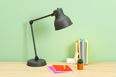 Photo of Stylish workplace with lamp, stationery and plant on wooden desk near light green wall