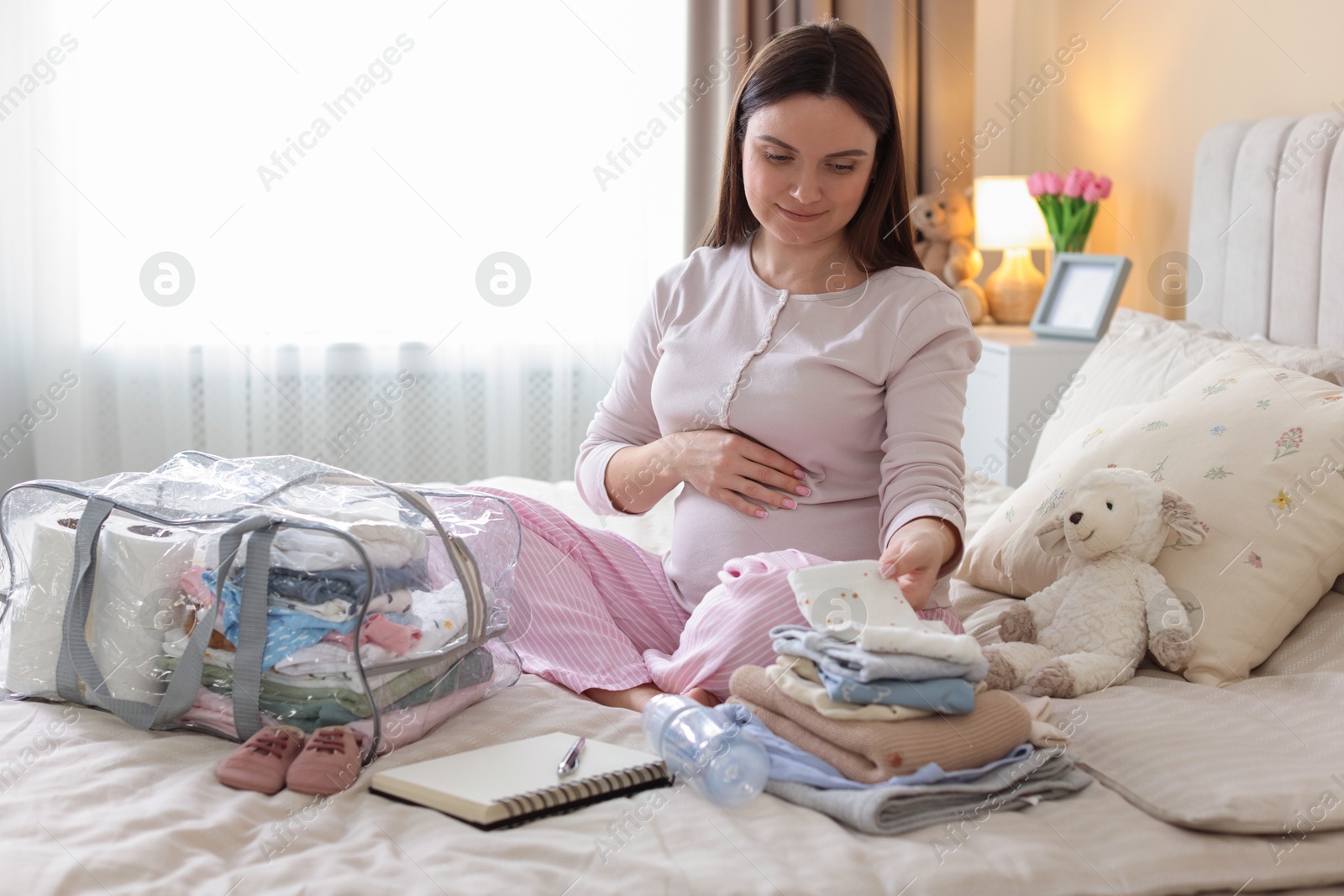 Pregnant woman packing baby stuff to bring into maternity hospital at home Photo of Pregnant woman packing baby stuff to bring into maternity hospital at home