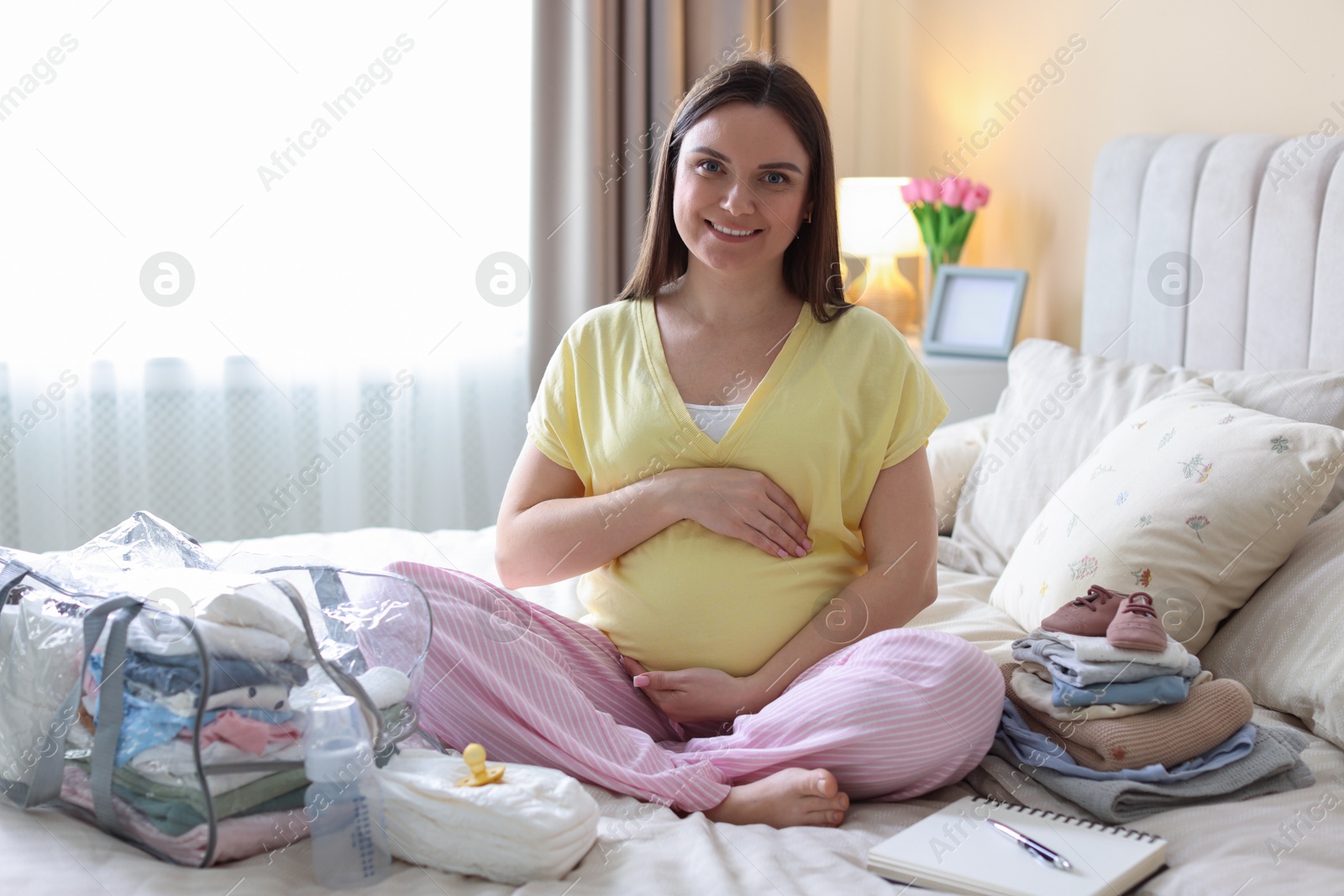 Pregnant woman on bed with baby stuff to bring into maternity hospital at home Photo of Pregnant woman on bed with baby stuff to bring into maternity hospital at home