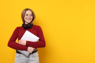 Photo of Smiling teenage girl with laptop on yellow background. Space for text