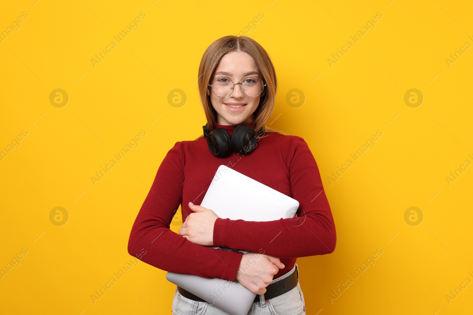 Photo of Smiling teenage girl with laptop on yellow background