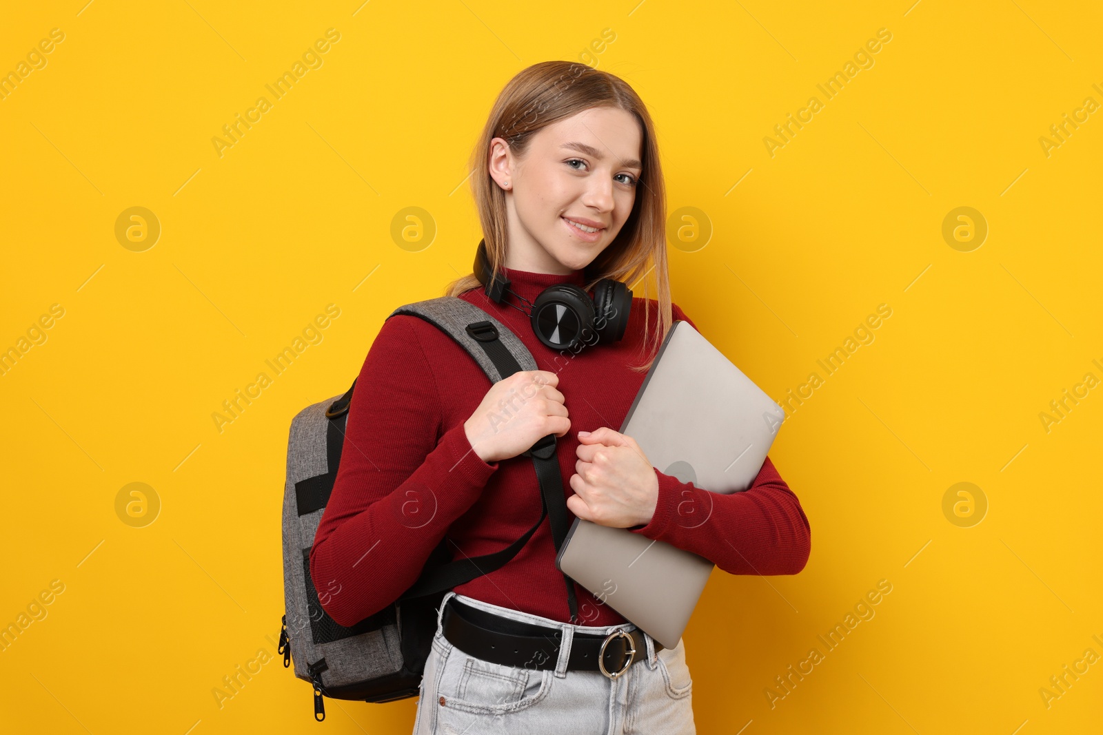 Smiling teenage girl with laptop on yellow background Photo of Smiling teenage girl with laptop on yellow background