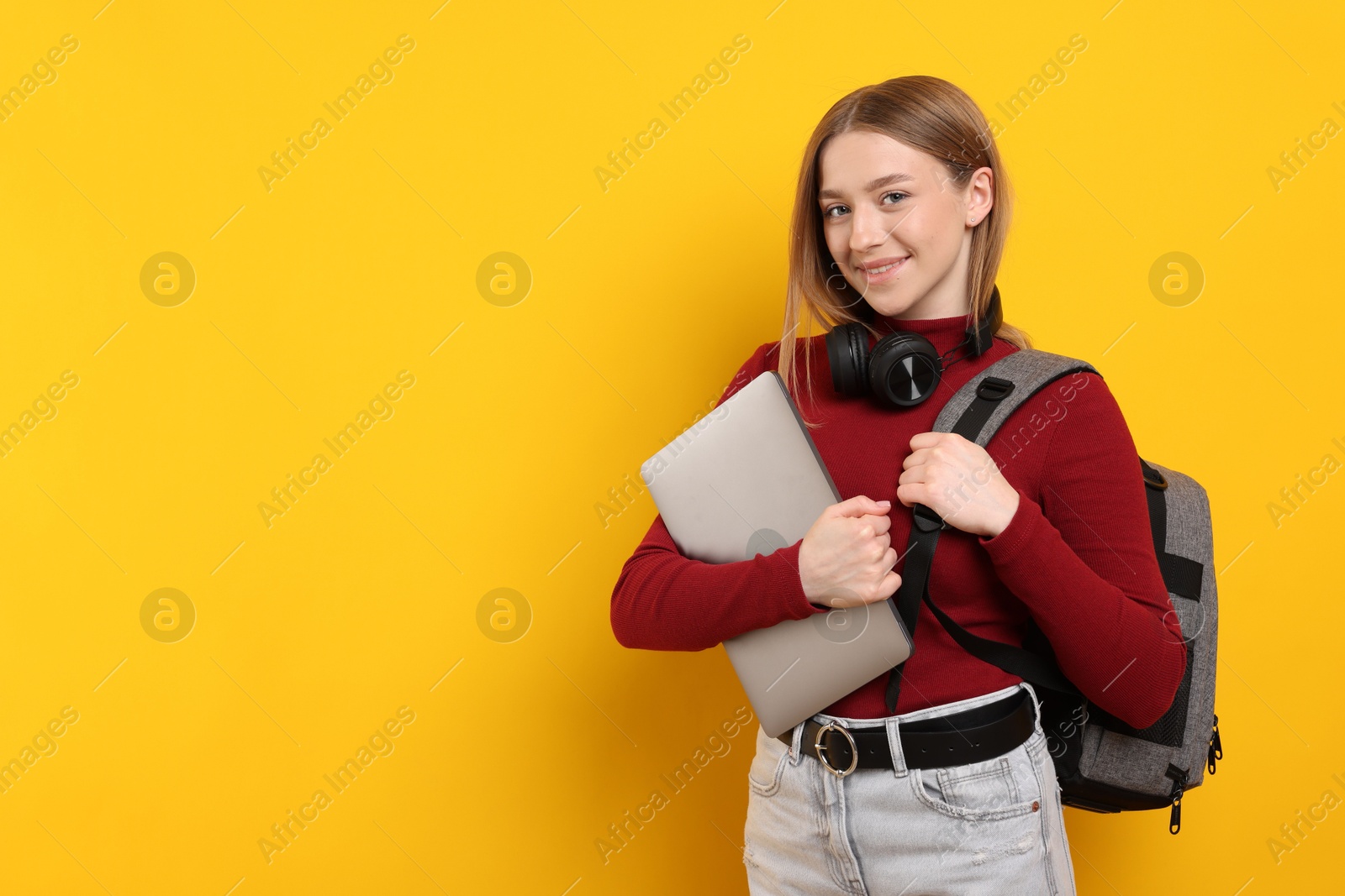 Smiling teenage girl with laptop on yellow background. Space for text Photo of Smiling teenage girl with laptop on yellow background. Space for text