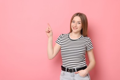 Photo of Portrait of smiling teenage girl pointing at something on pink background. Space for text