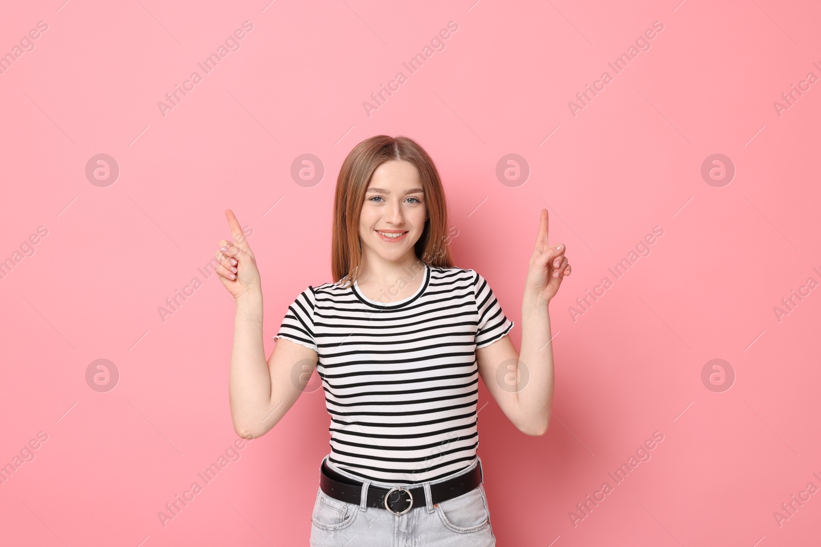 Portrait of smiling teenage girl pointing upwards on pink background Photo of Portrait of smiling teenage girl pointing upwards on pink background