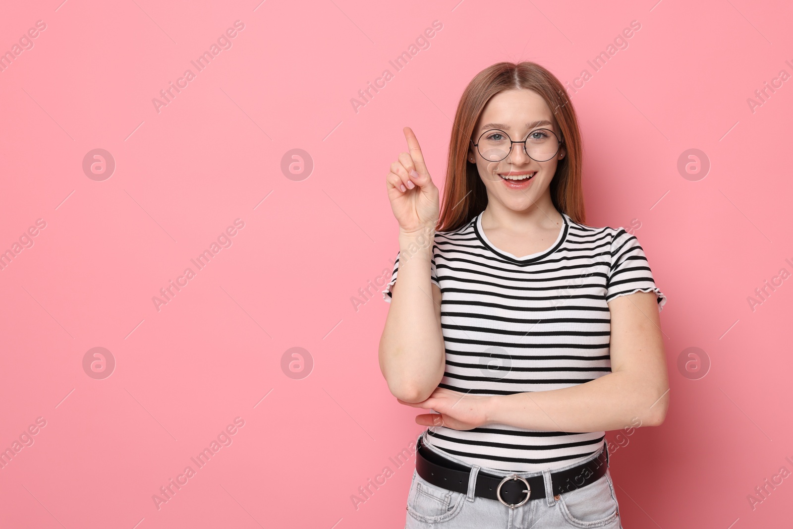Portrait of smiling teenage girl pointing upwards on pink background. Space for text Photo of Portrait of smiling teenage girl pointing upwards on pink background. Space for text