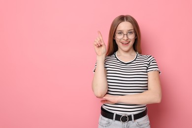 Photo of Portrait of smiling teenage girl pointing upwards on pink background. Space for text
