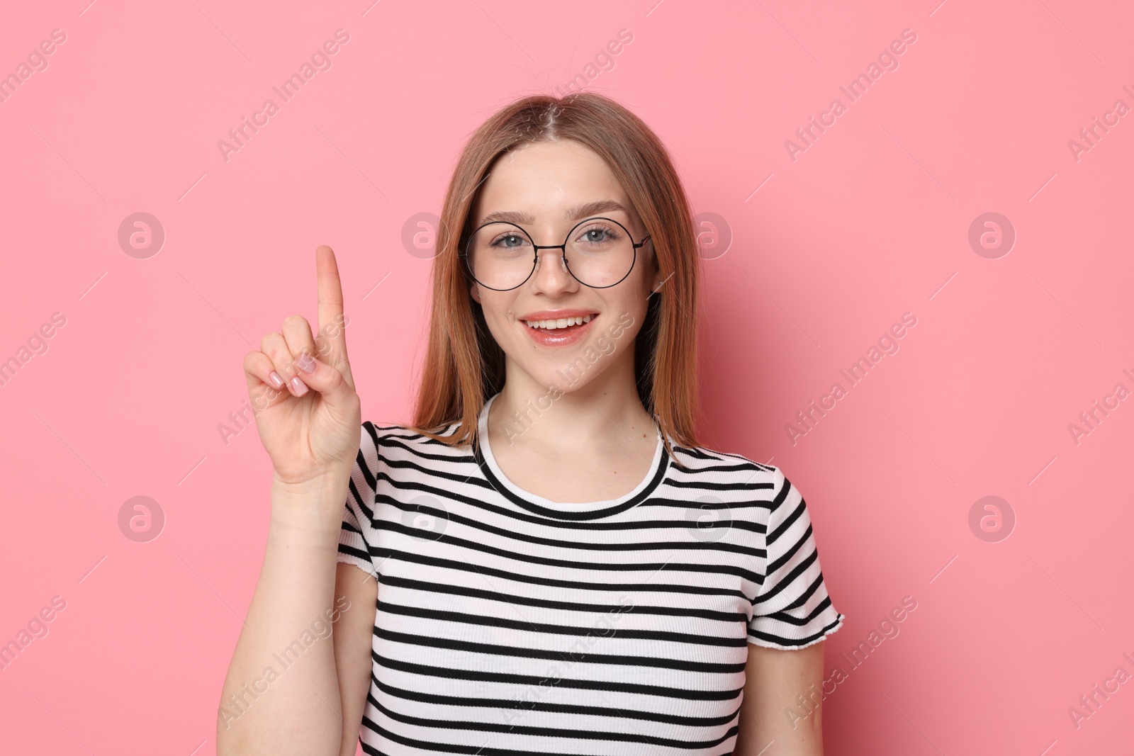Photo of Portrait of smiling teenage girl pointing upwards on pink background