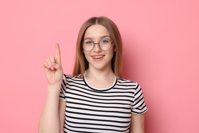 Photo of Portrait of smiling teenage girl pointing upwards on pink background