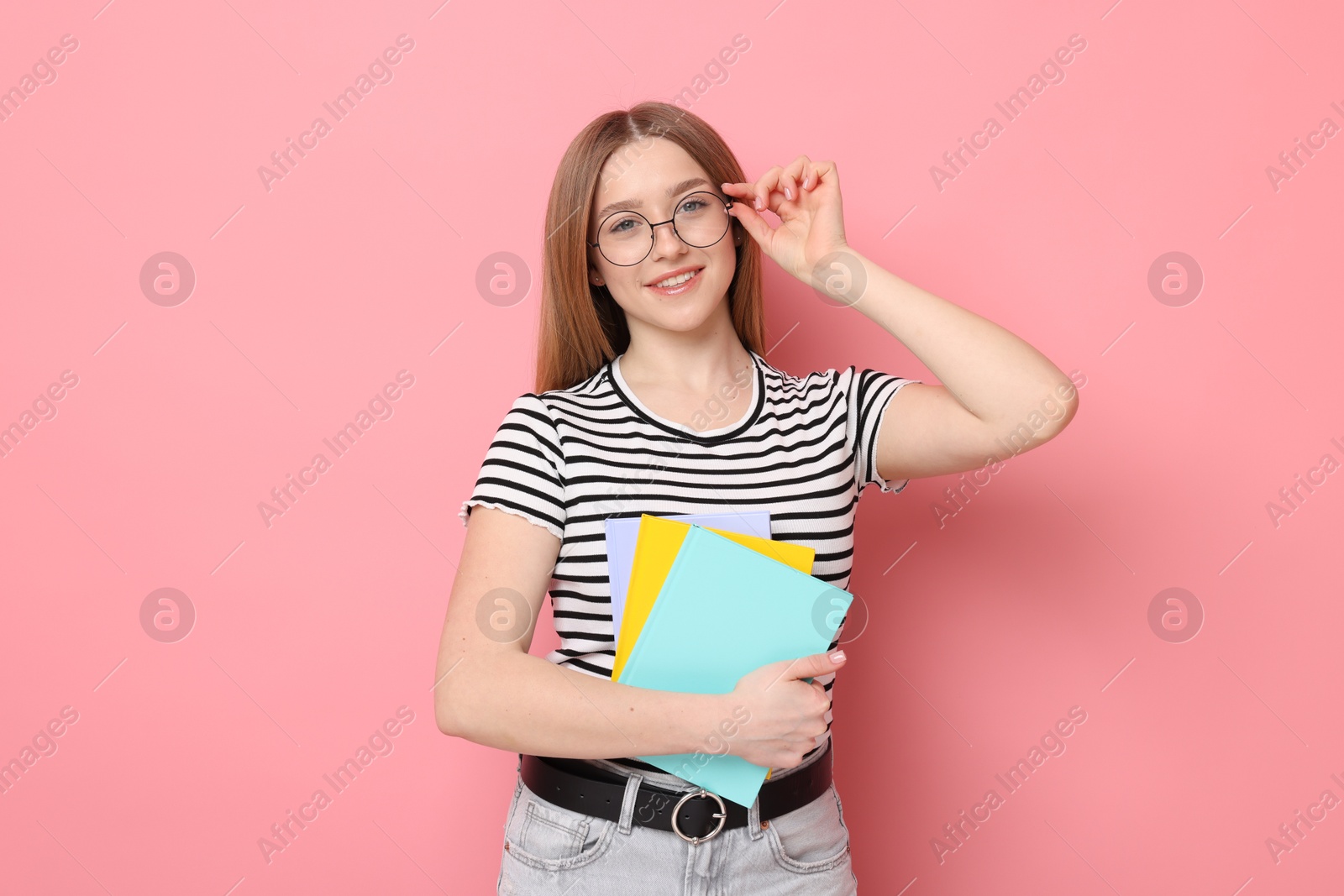 Photo of Portrait of smiling teenage girl with books on pink background