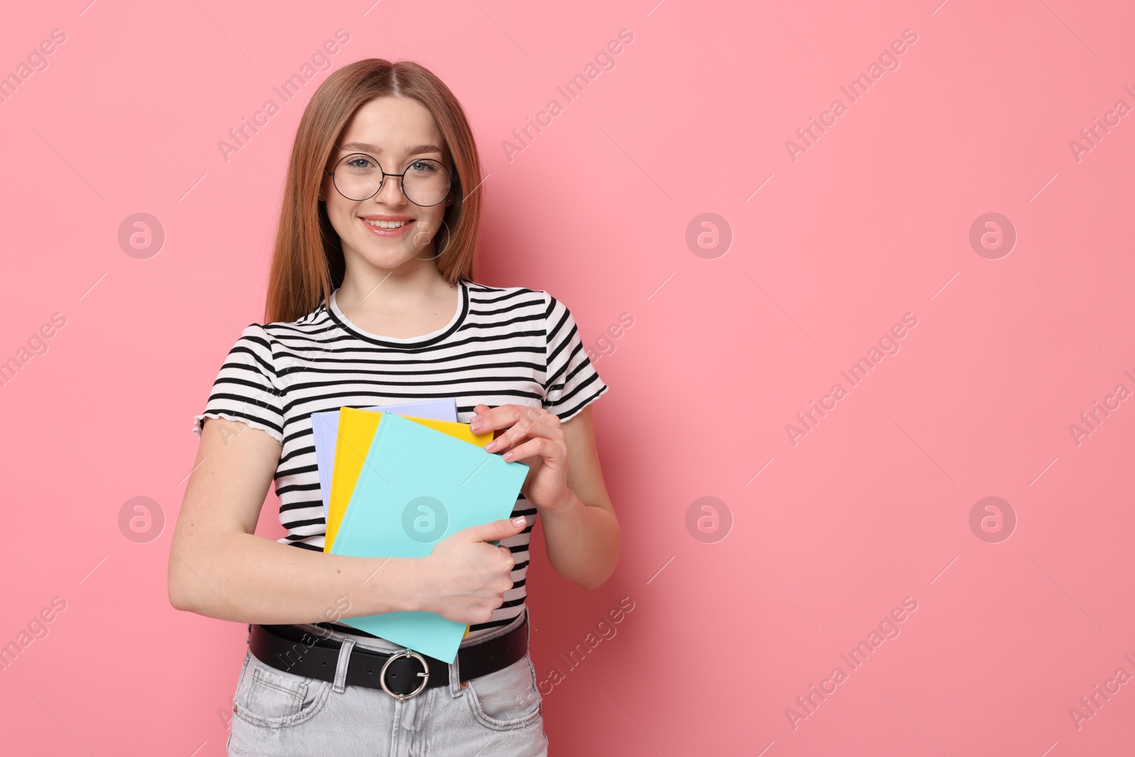 Photo of Portrait of smiling teenage girl with books on pink background. Space for text