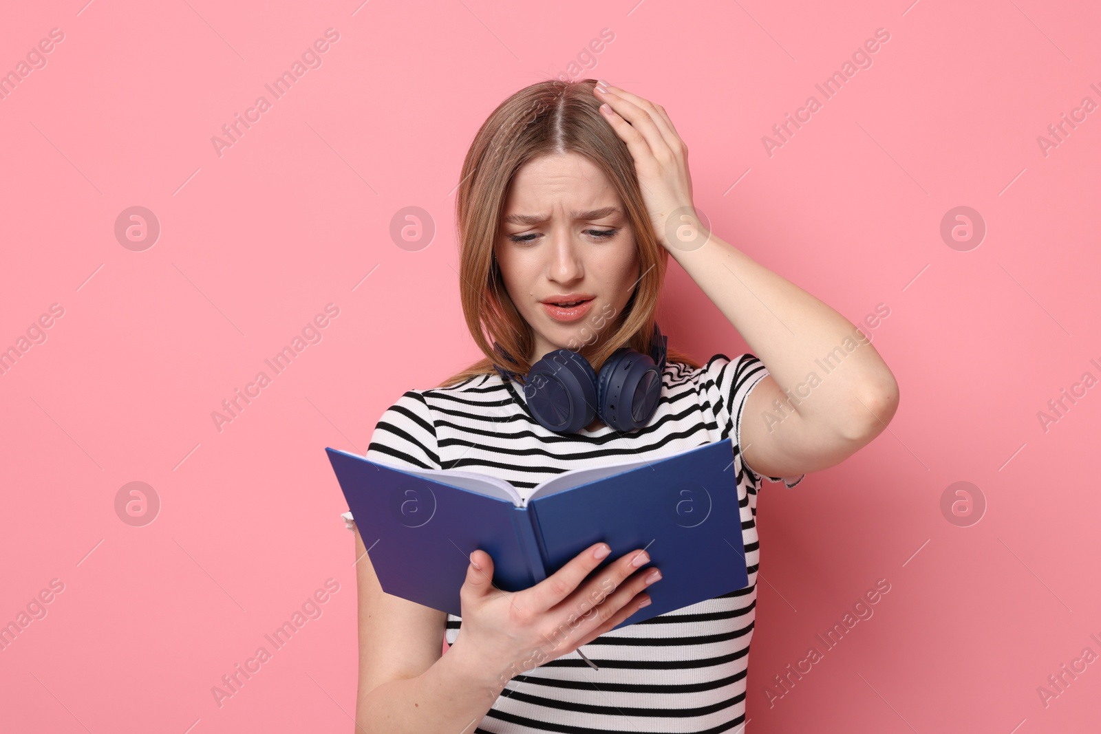 Emotional teenage girl with book on pink background Photo of Emotional teenage girl with book on pink background