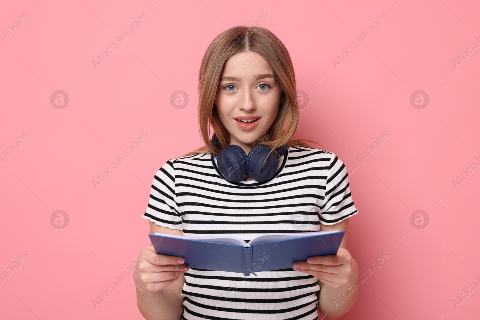 Emotional teenage girl with book on pink background Photo of Emotional teenage girl with book on pink background