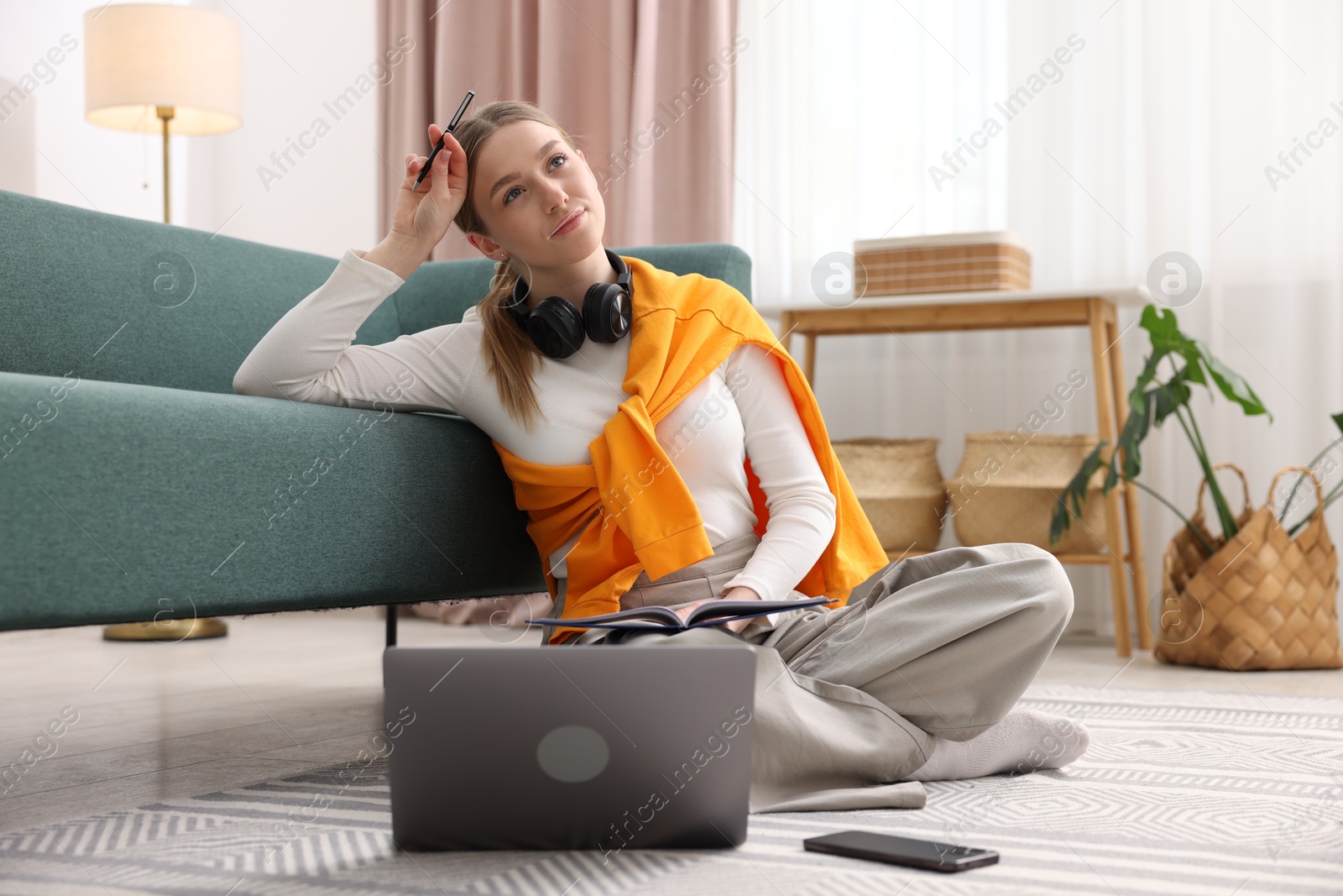 Photo of Teenage girl doing homework with book and laptop on floor at home