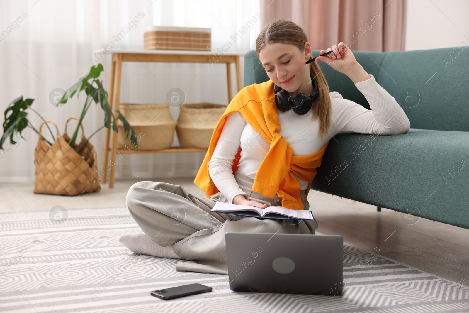Photo of Teenage girl doing homework with book and laptop on floor at home