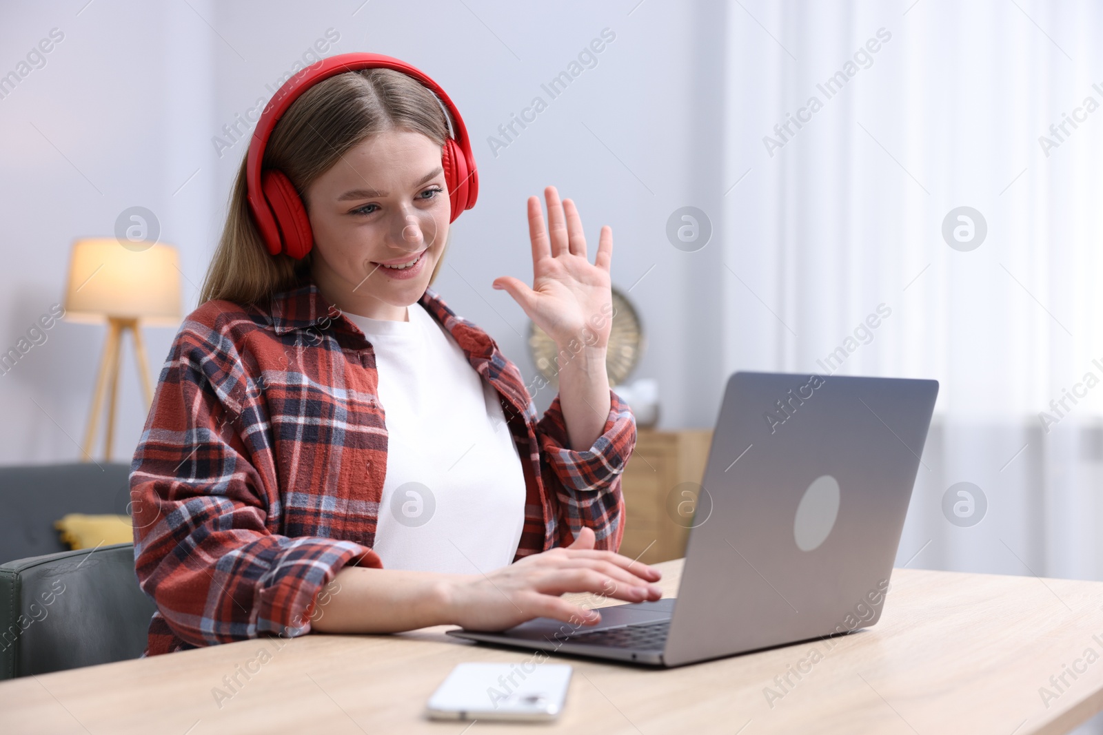 Smiling teenage girl having videochat by laptop at table indoors Photo of Smiling teenage girl having videochat by laptop at table indoors