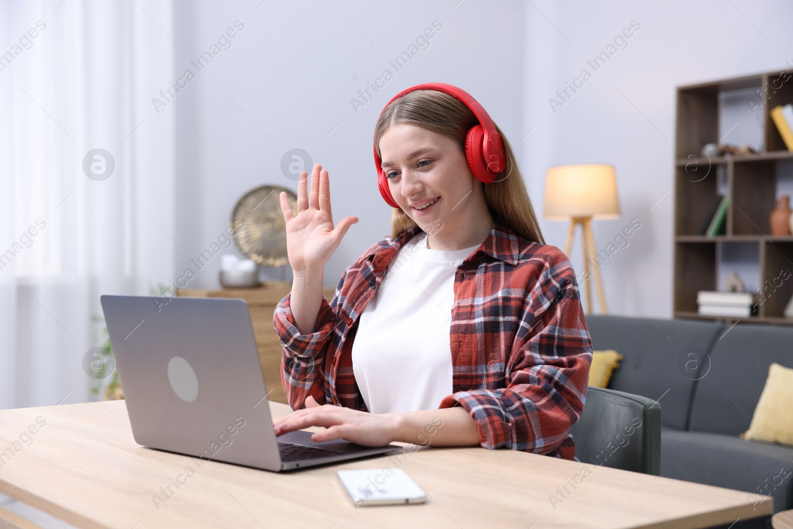 Smiling teenage girl having videochat by laptop at table indoors Photo of Smiling teenage girl having videochat by laptop at table indoors