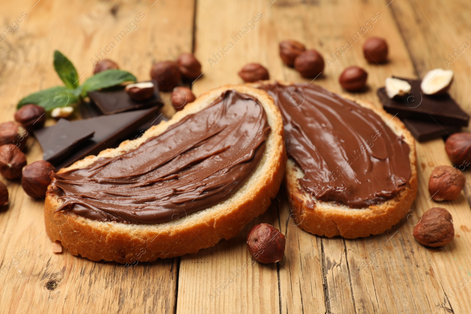 Toasts with tasty hazelnut spread, chocolate pieces and nuts on wooden table, closeup Photo of Toasts with tasty hazelnut spread, chocolate pieces and nuts on wooden table, closeup