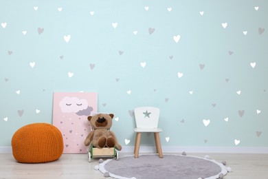 Image of Playroom interior. Small chair, ottoman, toys and picture near wall with cute wallpaper