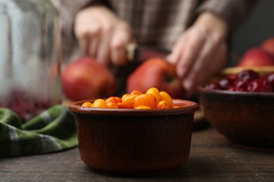 Photo of Woman cutting apples at wooden table, focus on sea buckthorn berries