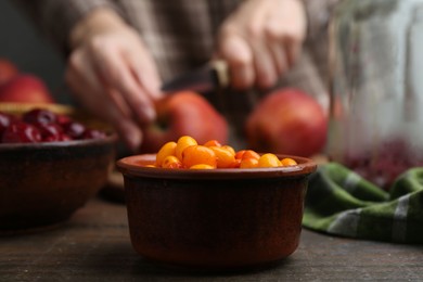 Photo of Woman cutting apples at wooden table, focus on sea buckthorn berries