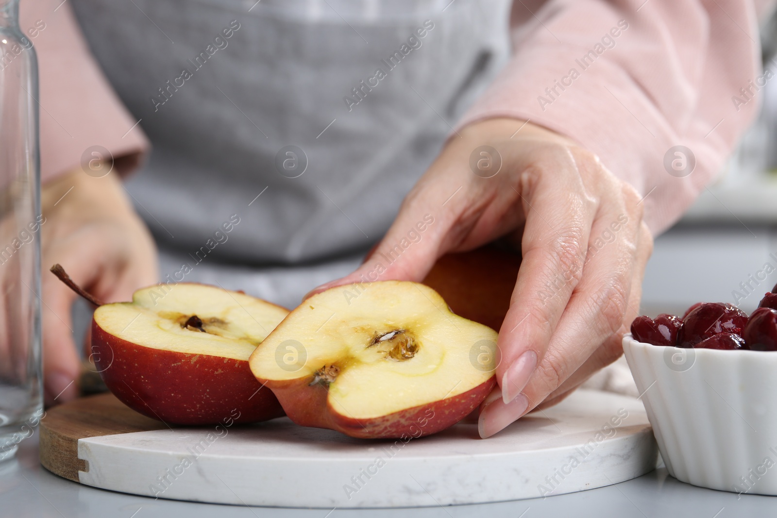 Photo of Woman with apples and cherries at light grey table, closeup