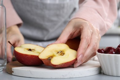 Photo of Woman with apples and cherries at light grey table, closeup