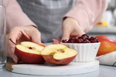 Photo of Woman with apples and cherries at light grey table, closeup