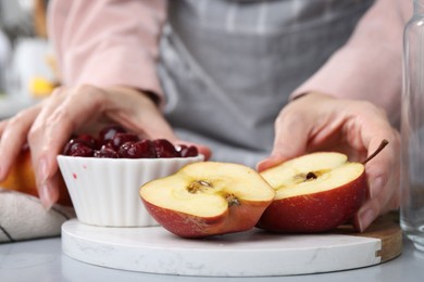 Photo of Woman with apples and cherries at light grey table, closeup