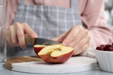 Photo of Woman cutting apples at light grey table, closeup