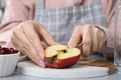 Photo of Woman cutting apples at light grey table, closeup