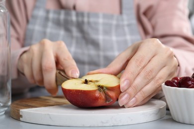 Photo of Woman cutting apples at light grey table, closeup