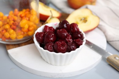 Photo of Tasty cherries, apples and sea buckthorn berries on light grey table, closeup