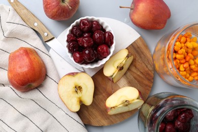 Photo of Tasty cherries, apples and sea buckthorn berries on light grey table, flat lay