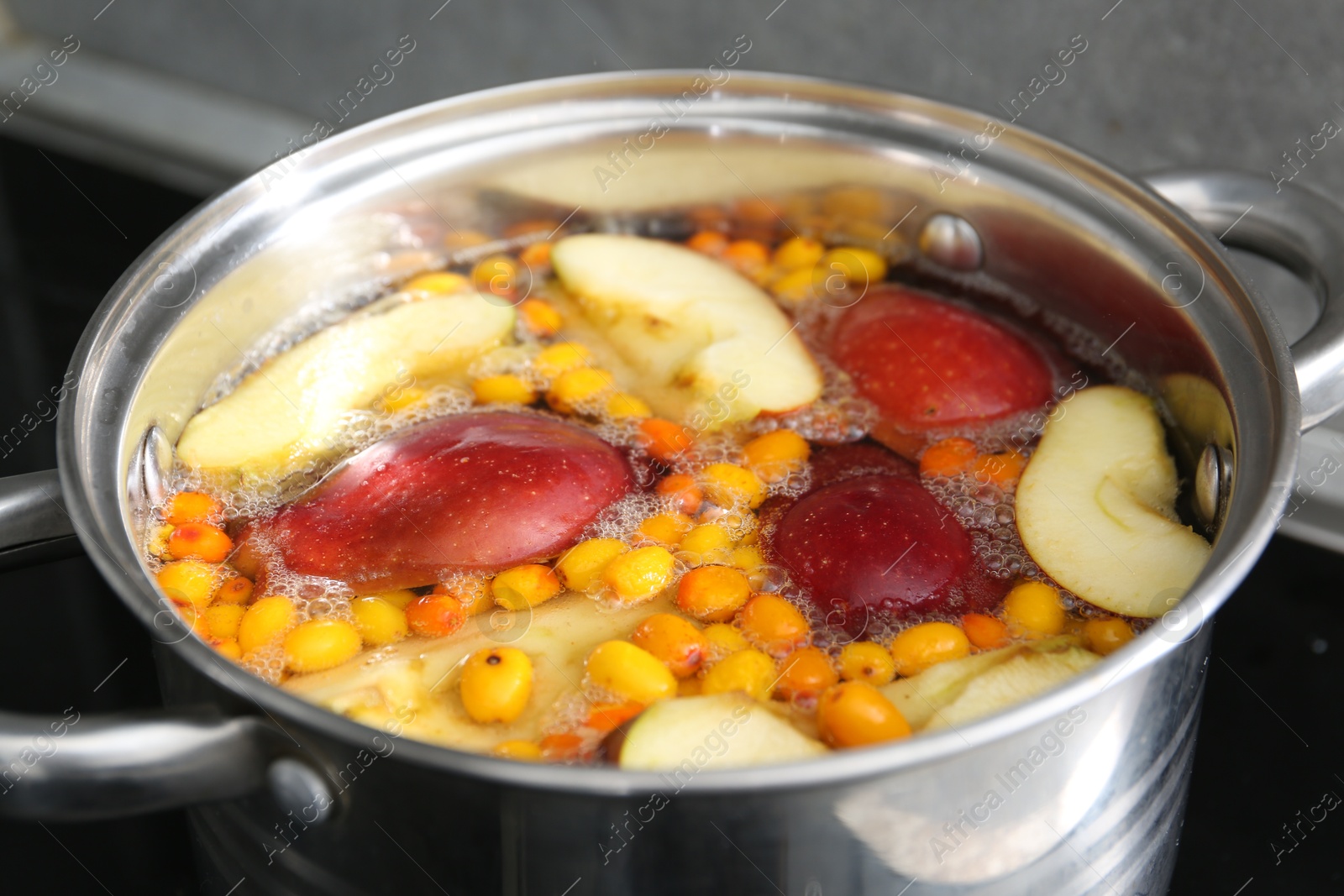 Making compot of apples and sea buckthorn berries. Simmering fruits in pot on stove, closeup Photo of Making compot of apples and sea buckthorn berries. Simmering fruits in pot on stove, closeup