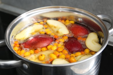 Photo of Making compot of apples and sea buckthorn berries. Simmering fruits in pot on stove, closeup