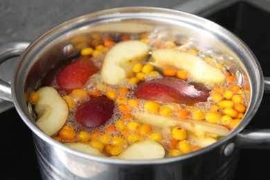Photo of Making compot of apples and sea buckthorn berries. Simmering fruits in pot on stove, closeup
