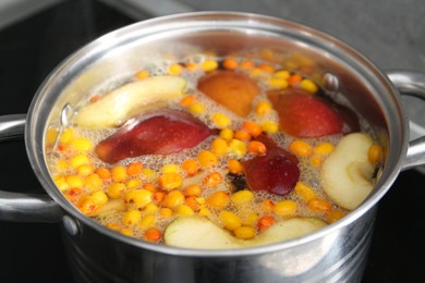 Photo of Making compot of apples and sea buckthorn berries. Simmering fruits in pot on stove, closeup