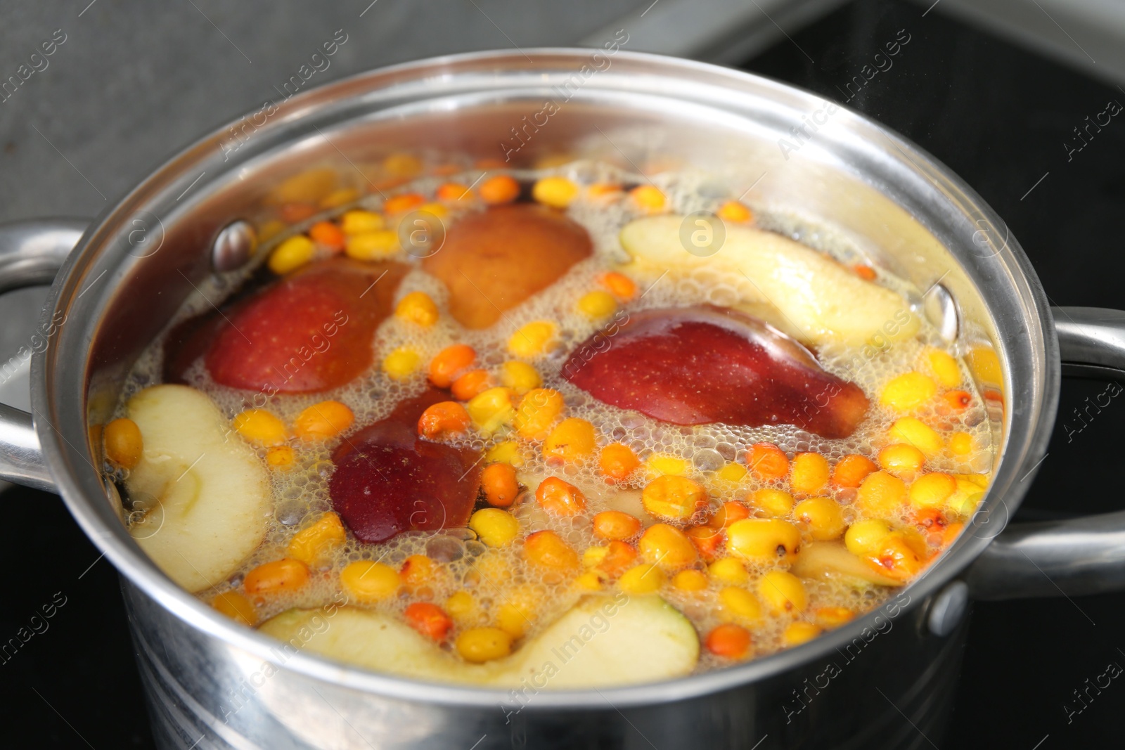 Photo of Making compot of apples and sea buckthorn berries. Simmering fruits in pot on stove, closeup
