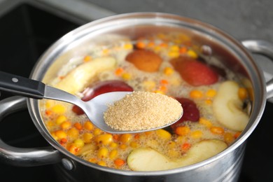 Photo of Adding sugar into tasty compot in pot on stove, closeup