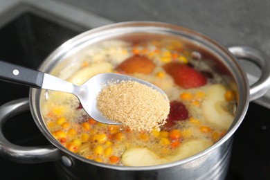 Photo of Adding sugar into tasty compot in pot on stove, closeup